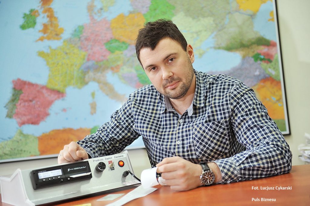 Kamil Wolański ekspert OCRK z tachografem na tle mapy.